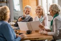 Happy mature friends talking about their memories while looking at photo album at home. &copy;Freepik